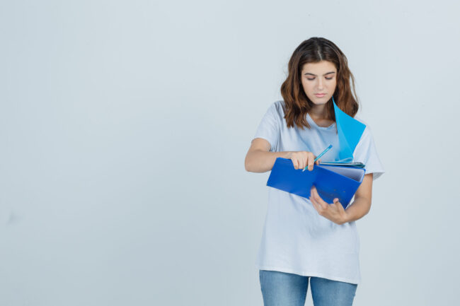 young female looking over notes on folders in white t-shirt, jeans and looking focused , front view.